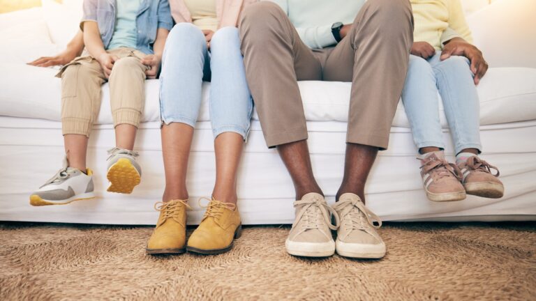 Personen verschiedener Generationen sitzen auf einer Couch. Im Fokus sind ihre Füße und Schuhe zu sehen.