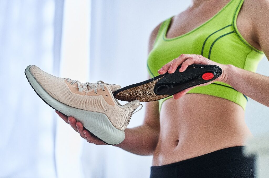 Fitness-Frau mit weichen orthopädischen Einlegesohlen und Turnschuhen für Lauftraining und Jogging. Behandlung und Vorbeugung von Plattfüßen und Fußkrankheiten, Unterstützung des Fußgewölbes. Bequeme Sportschuhe tragen