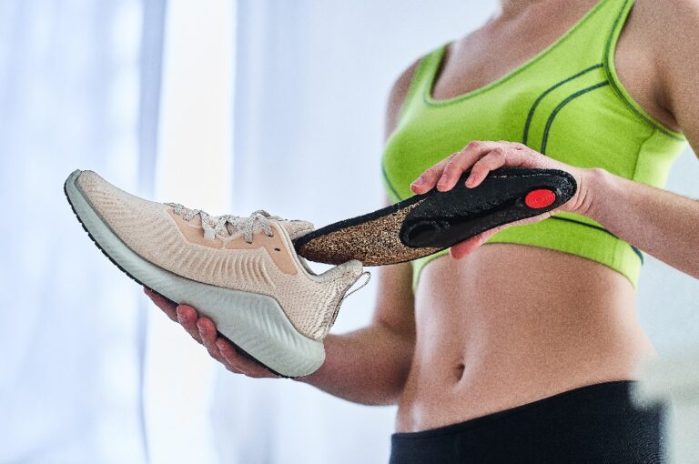 Fitness-Frau mit weichen orthopädischen Einlegesohlen und Turnschuhen für Lauftraining und Jogging. Behandlung und Vorbeugung von Plattfüßen und Fußkrankheiten, Unterstützung des Fußgewölbes. Bequeme Sportschuhe tragen