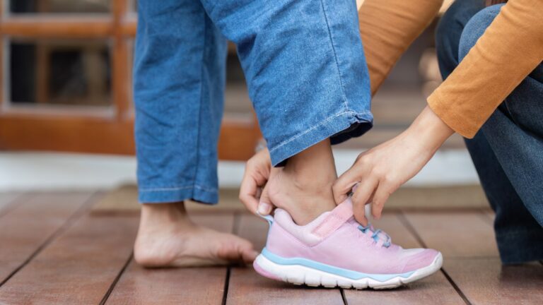 Vorbereitungen für den Schulanfang. Ein Kind bereitet sich auf die Schule vor, während ein fürsorglicher Erwachsener ihm die Schuhe anzieht.